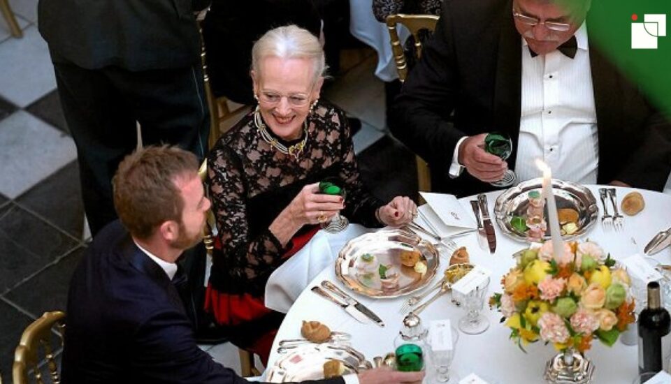 Formal dining event with well-dressed guests seated at a round table, enjoying a meal in perfect rhythm. Silver cutlery, white linens, and floral centerpieces enhance the elegant ambiance.