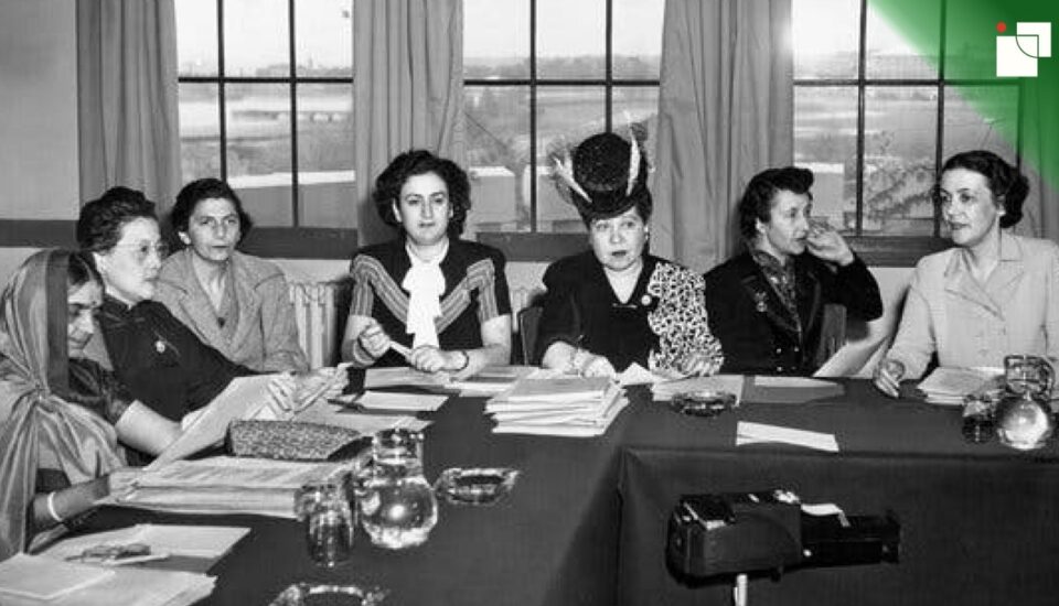 Black-and-white photo of seven influential women seated around a table during a mid-20th-century diplomatic meeting. They wear formal attire, some with hats and traditional dress, representing early female involvement in international diplomacy.