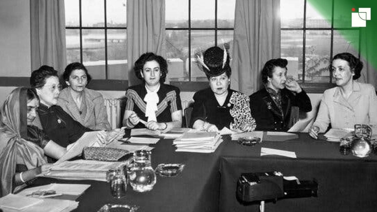 Black-and-white photo of seven influential women seated around a table during a mid-20th-century diplomatic meeting. They wear formal attire, some with hats and traditional dress, representing early female involvement in international diplomacy.